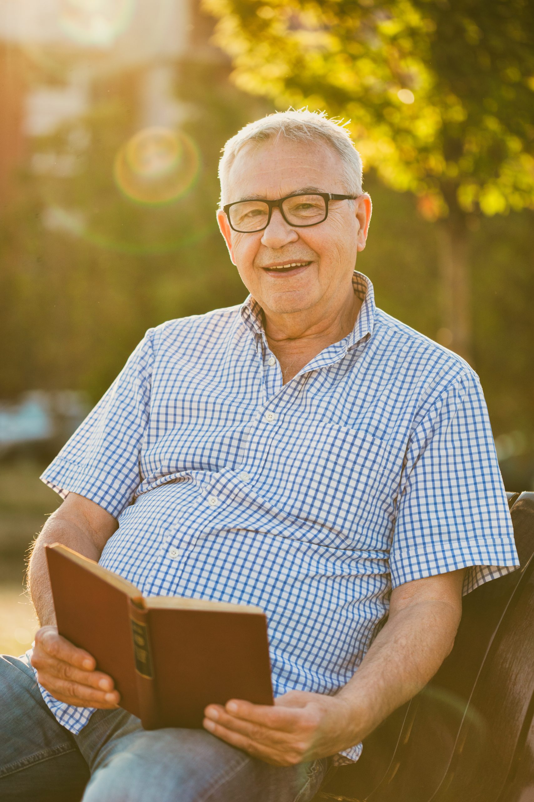 Outdoor portrait of happy senior man who is reading book.