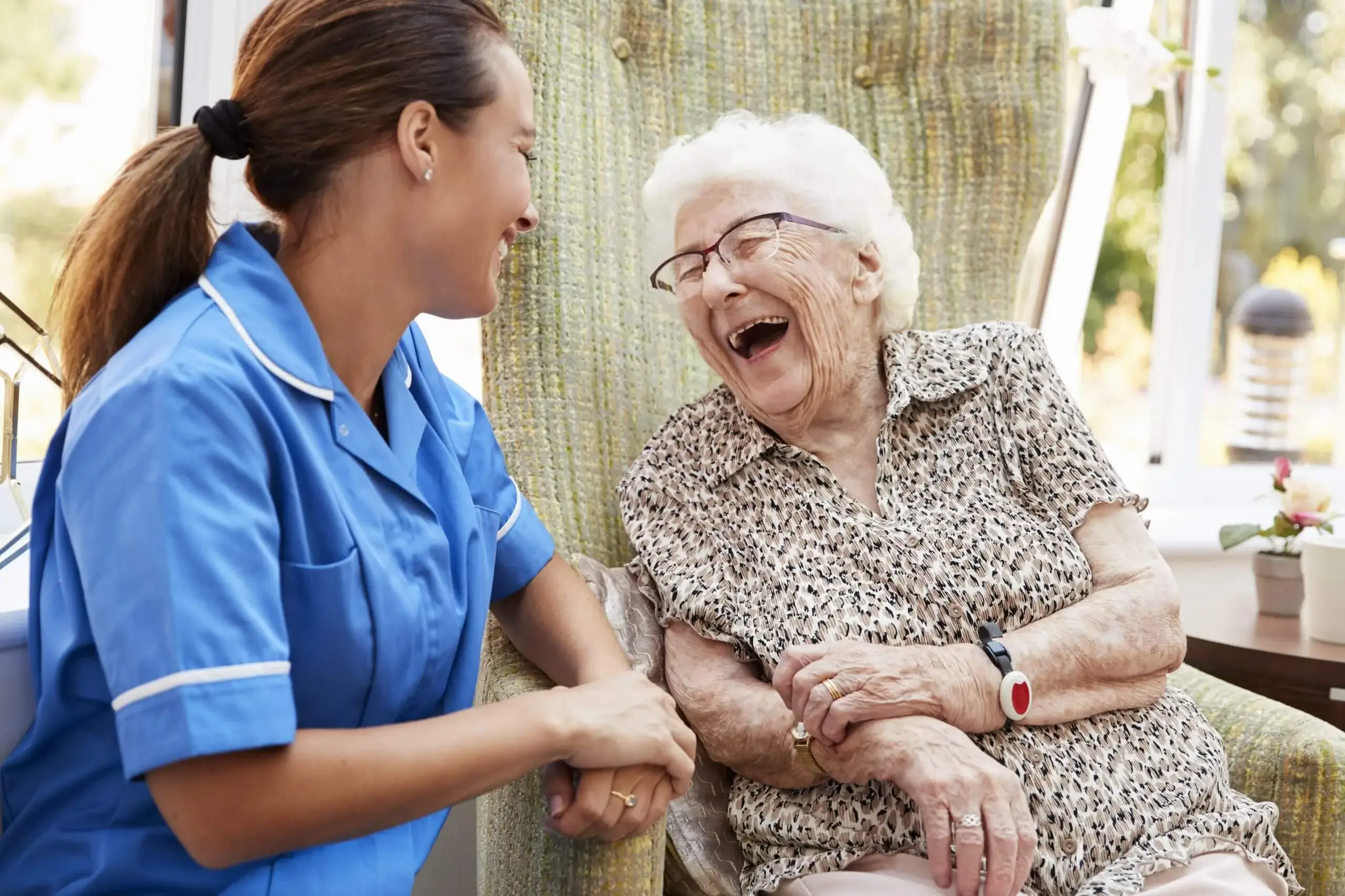 Senior Woman Sitting In Chair And Laughing With Nurse at assisted living oakville ontario
